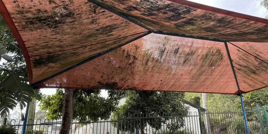 Before – red outdoor park shade sail heavily covered in mould